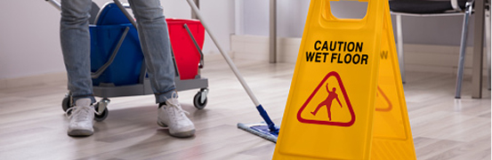 someone cleaning a floor along a wet floor sign